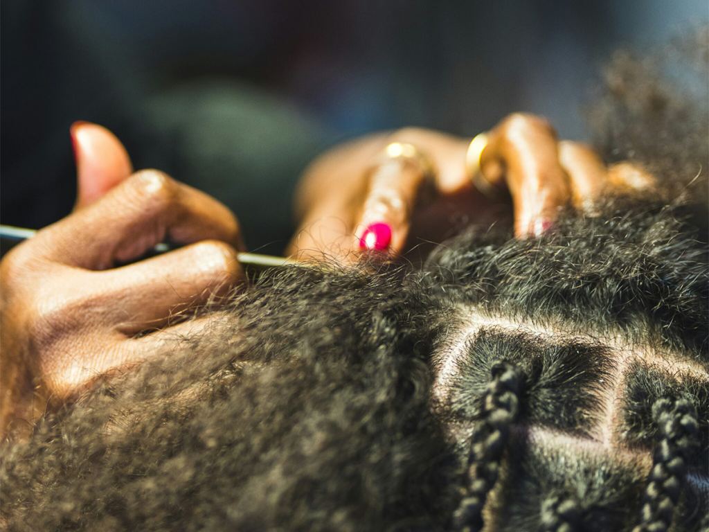 Close-up of hands braiding textured hair, with a metal tool parting the hair into neat sections. Some braids are already completed. - PsychDiscouse