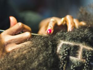 Close-up of hands braiding textured hair, with a metal tool parting the hair into neat sections. Some braids are already completed. - PsychDiscouse