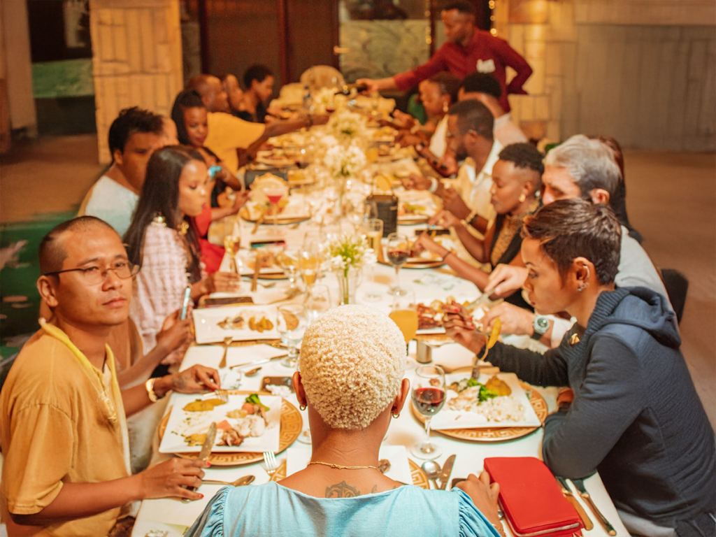 A large group of people sit around a long table, sharing a meal together in a warmly lit indoor setting. - PsychDiscouse