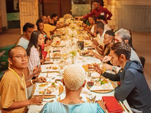 A large group of people sit around a long table, sharing a meal together in a warmly lit indoor setting. - PsychDiscouse