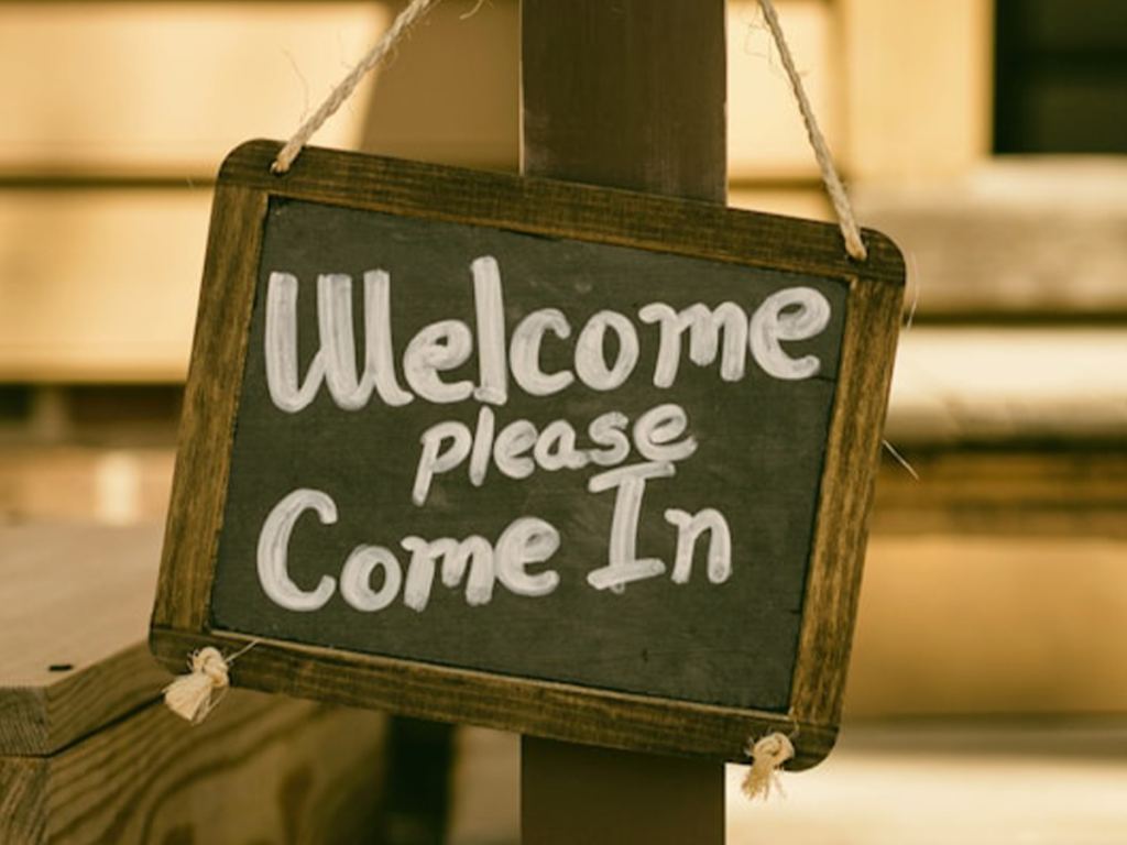 A chalkboard sign hanging on a post reads "Welcome please Come In" in white handwritten letters. - PsychDiscouse