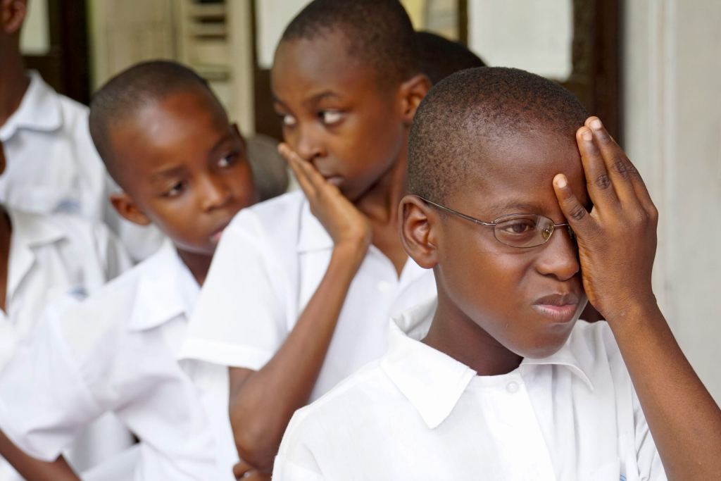 Three boys in white shirts stand in line; the boy in front covers one eye with his hand, while the others watch. - PsychDiscouse