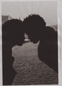 Two people with curly hair are silhouetted, facing each other closely with their foreheads touching, against a background of cobblestones and an out-of-focus urban setting. - PsychDiscouse