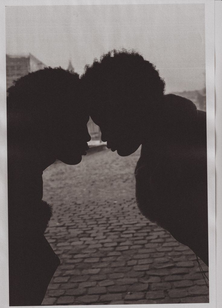 Two people with curly hair are silhouetted, facing each other closely with their foreheads touching, against a background of cobblestones and an out-of-focus urban setting. - PsychDiscouse
