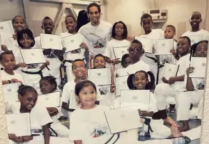 A group of children in martial arts uniforms sit and stand together, holding certificates, with an adult instructor in the center. - PsychDiscouse