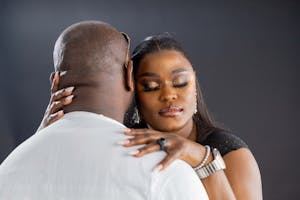 A woman embraces a man, eyes closed, resting her head on his shoulder. The man faces away from the camera, both wearing formal attire against a dark background. - PsychDiscouse