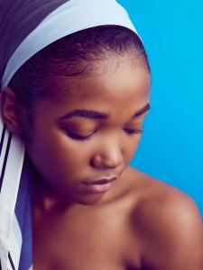 A woman with a headscarf looks downward with her eyes closed against a bright blue background. - PsychDiscouse