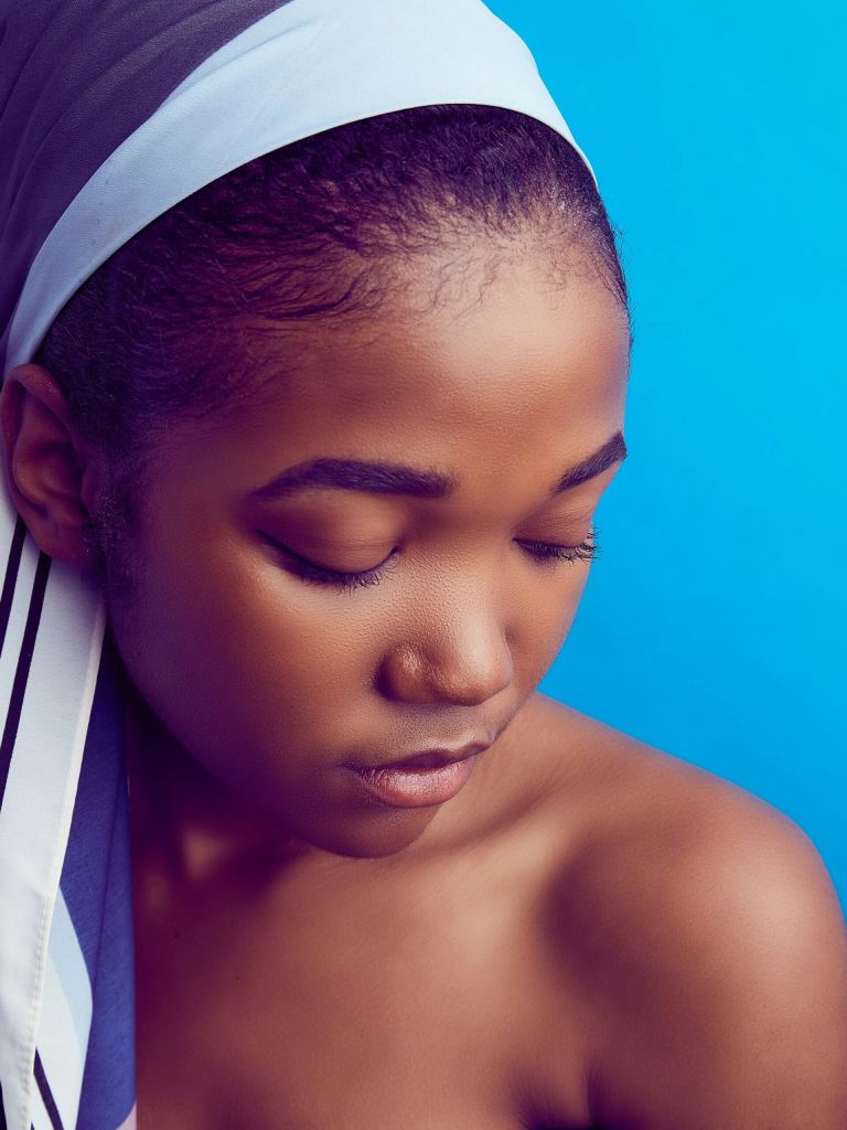 A woman with a headscarf looks downward with her eyes closed against a bright blue background. - PsychDiscouse
