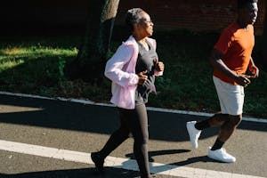 Two people jog outdoors on a paved path; one wears a pink jacket and black pants, the other wears a red shirt and white shorts. - PsychDiscouse