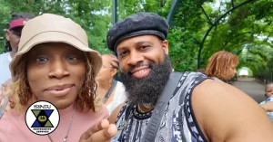 A woman in a bucket hat and a man with a beard and black beret pose for a selfie in a park, with an “ISINTU Restorative Services” logo in the corner. - PsychDiscouse