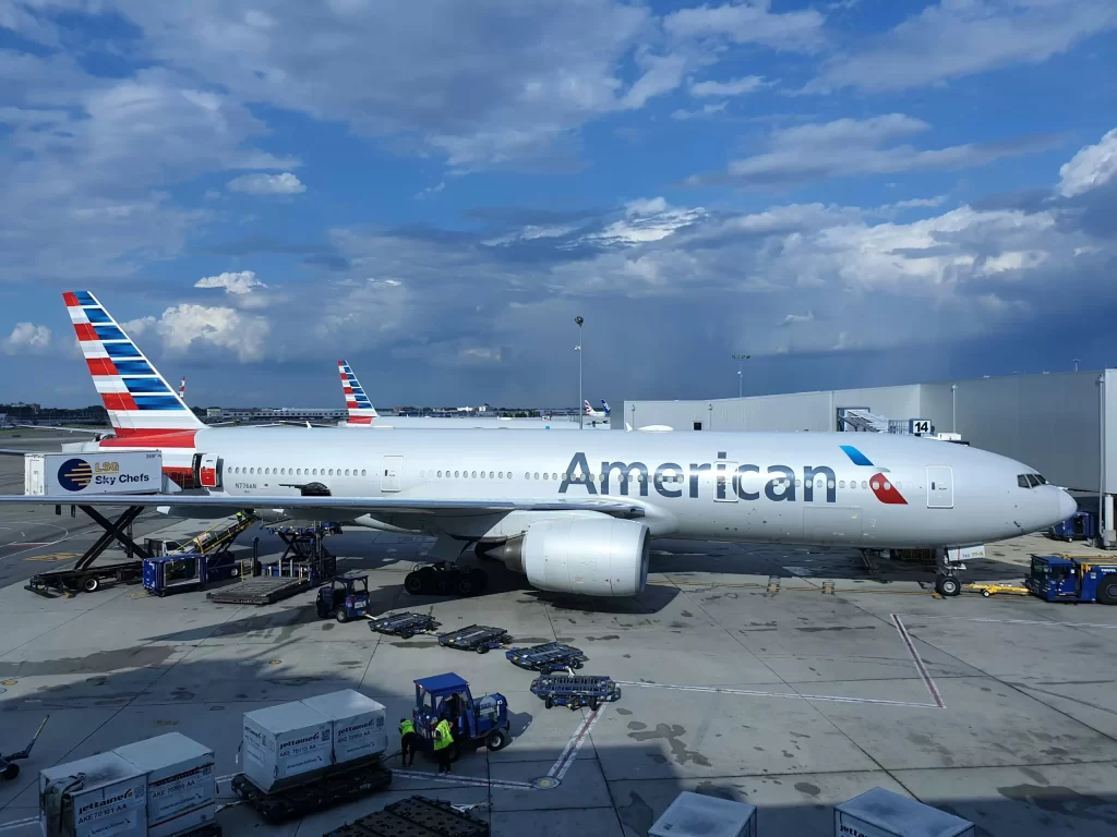 An American Airlines passenger jet parked at an airport gate being serviced by ground crew and equipment. - PsychDiscouse