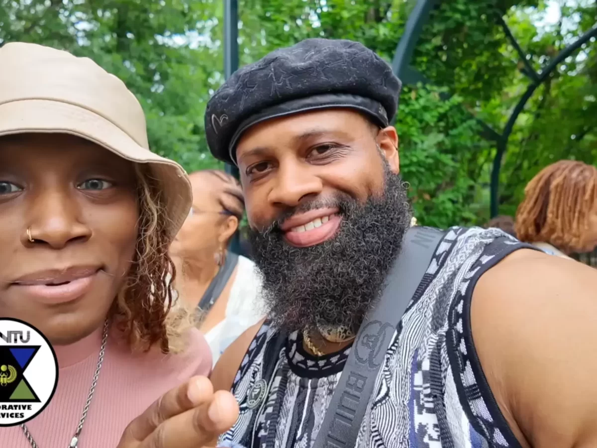 A woman in a bucket hat and a man with a beard and black beret pose for a selfie in a park, with an “ISINTU Restorative Services” logo in the corner. - PsychDiscouse