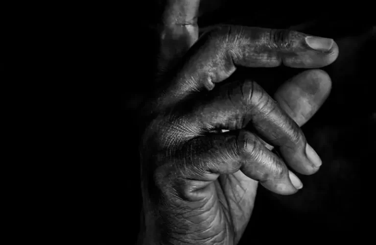 Black and white close-up of a person holding a finger to their lips in a gesture for silence. - PsychDiscouse