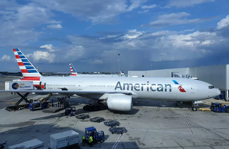 An American Airlines passenger jet parked at an airport gate being serviced by ground crew and equipment. - PsychDiscouse