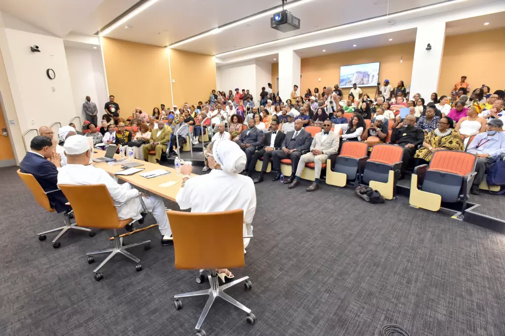 A panel of four people in white uniforms speaks to a seated audience in a lecture hall, with a screen displaying an image behind them. - PsychDiscouse