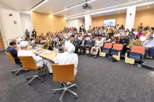 A panel of four people in white uniforms speaks to a seated audience in a lecture hall, with a screen displaying an image behind them. - PsychDiscouse