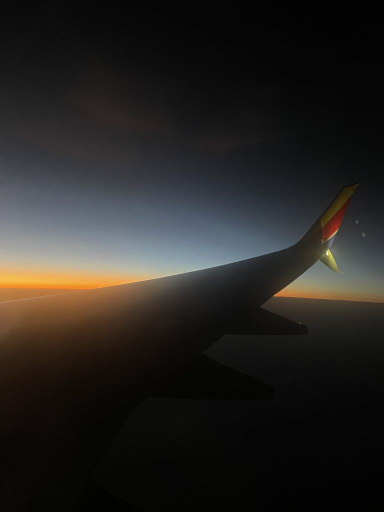 View from an airplane window showing a wing and a colorful sunset or sunrise sky with a gradient from orange to deep blue. - PsychDiscouse