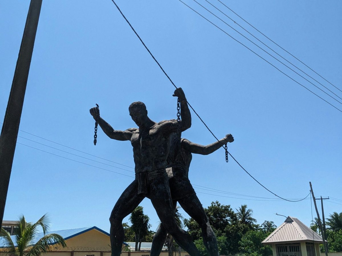 Bronze sculpture of two figures holding broken chains, standing on a raised platform outdoors, with buildings, trees, and a clear blue sky in the background. - PsychDiscouse
